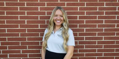 Smiling woman with long blonde hair standing against a brick wall.