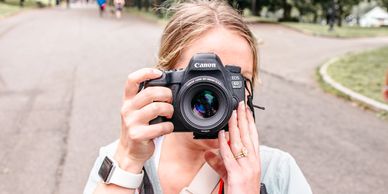 Person holding a Canon camera, taking a photo outdoors.