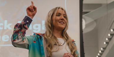 Woman giving a presentation with a confident expression and raised hand.