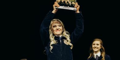 Woman holding a trophy triumphantly on stage.