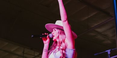 Female singer in a hat performing on stage with a microphone.