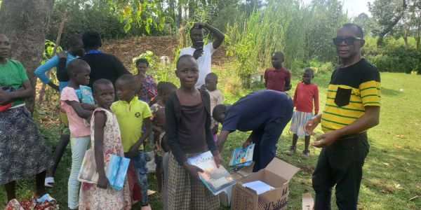 Group of children receiving books outdoors.