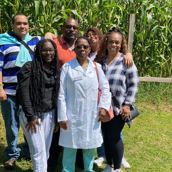 Group of six people posing outdoors near corn stalks.