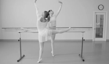 Two ballet dancers practicing at the barre in a studio.