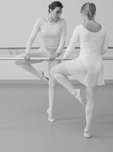 Two women practicing ballet at a barre in a dance studio.