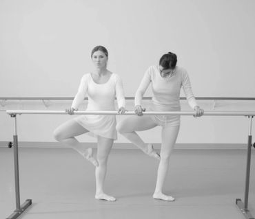 Two women practicing ballet at a barre in a dance studio.