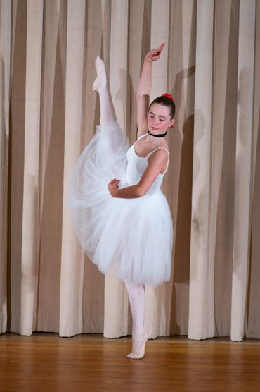 Ballet dancer in white tutu performing a high leg lift on stage.