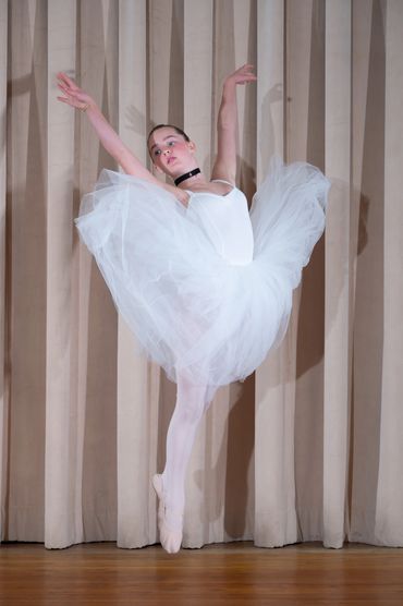 Ballet dancer in white tutu performing on stage.
