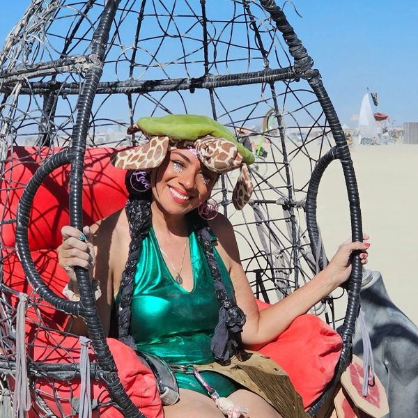 Woman in a unique outfit sitting in a hanging chair outdoors.
