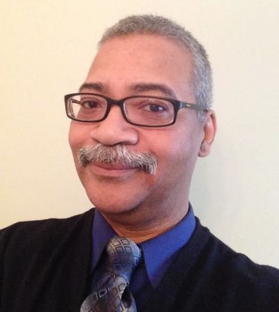 Smiling man with glasses and mustache wearing a blue shirt and patterned tie.