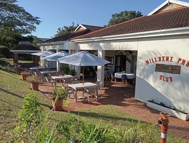 Outdoor seating area with umbrellas at Milldene Park Club on a sunny day.