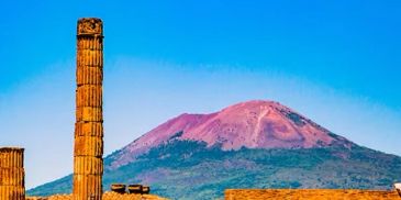 Ruins in front of a volcano under a clear blue sky.