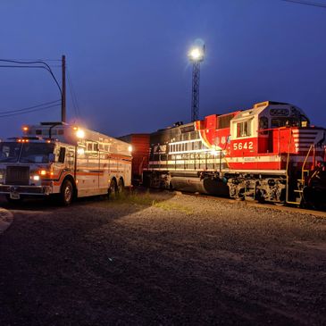 Nighttime scene with a red and black locomotive and a white service truck under bright lights.