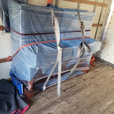 Moving blanket and shrink-wrapped Piano Secured to a Piano board in a moving truck Tied down