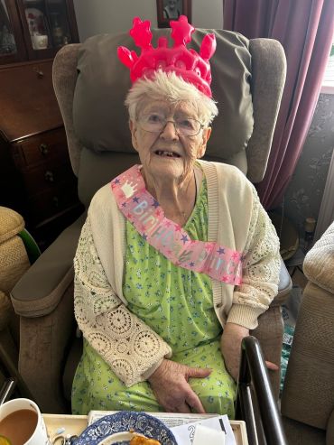 Elderly woman wearing a birthday sash and hat.