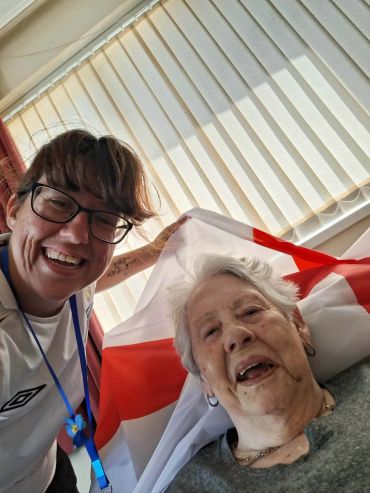 Two women smiling, one elderly, with a flag.