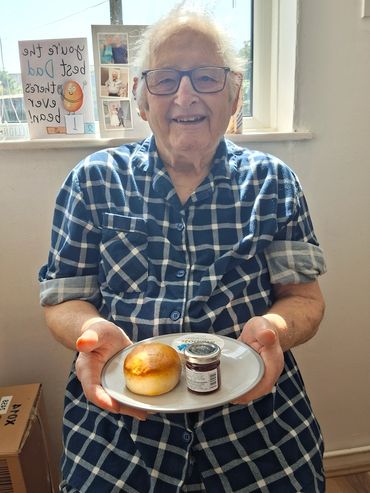 Elderly man holding a plate with bread and jam.