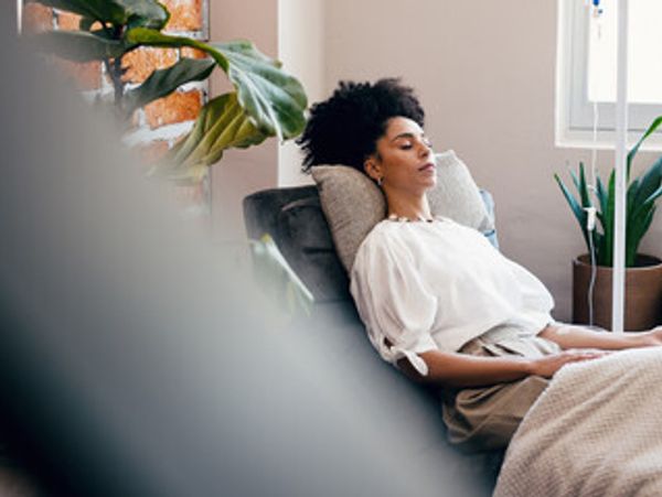 A woman relaxes on a couch with her eyes closed in a cozy, plant-filled room.