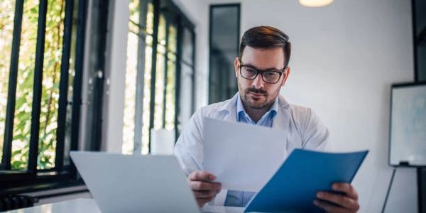 Man in glasses reviewing documents at a desk with a laptop.