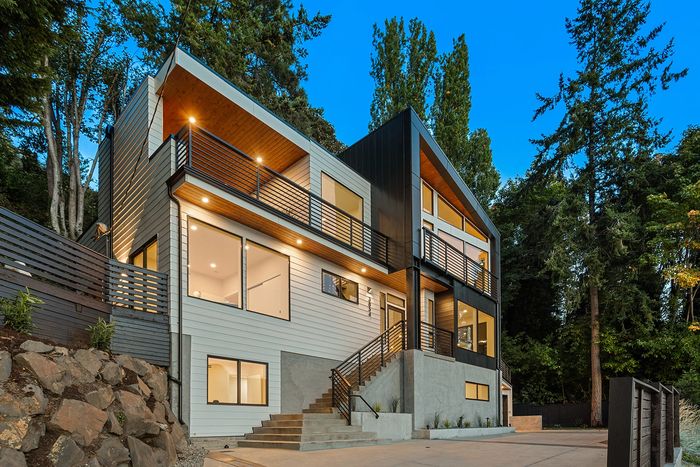 Modern two-story house with large windows and outdoor lighting at dusk.
