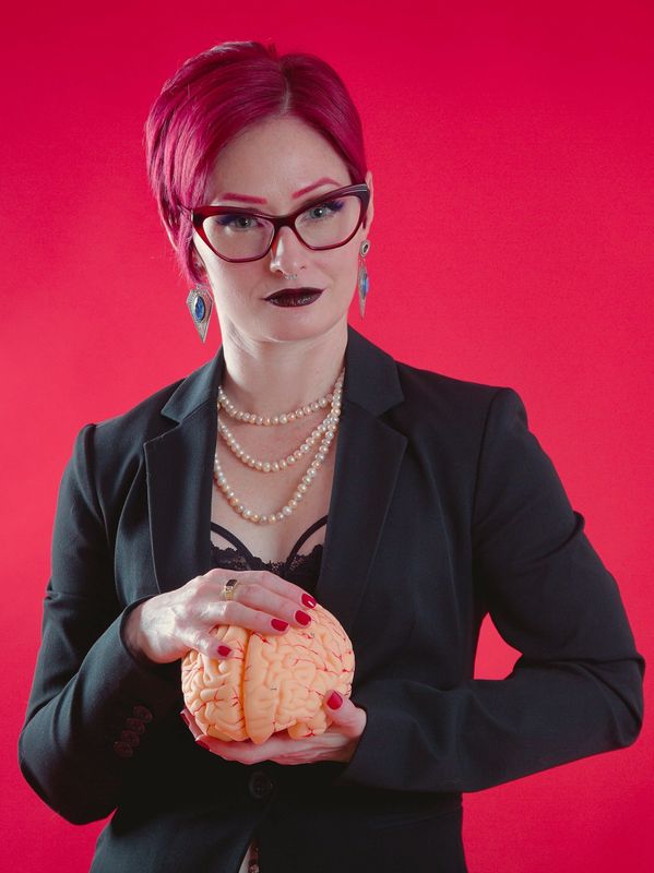 Woman with red hair holding a brain model against a red background.