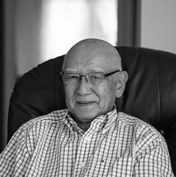 Elderly man wearing glasses sitting on a chair.