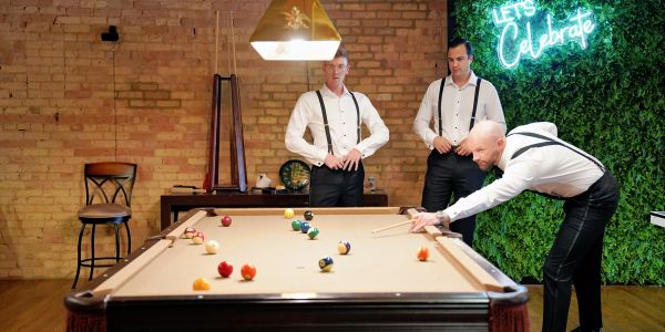 Three men in suspenders playing pool in a stylish room.