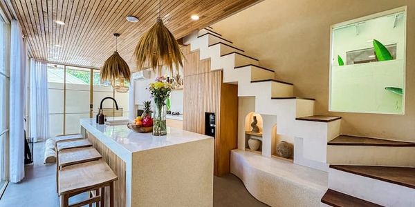Modern kitchen with island, wooden stools, and staircase seating area.