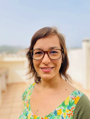 Smiling woman with glasses in a colorful floral top outdoors.