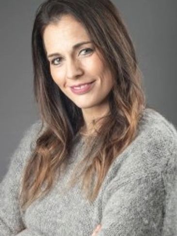 Smiling woman with long brown hair wearing a cozy gray sweater.