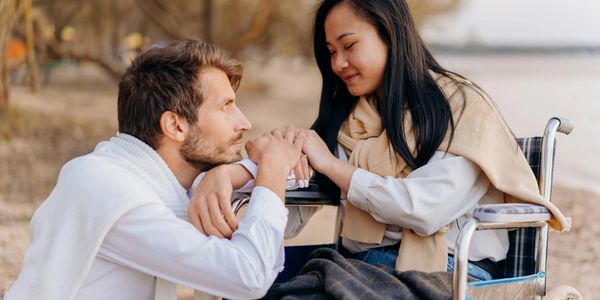 Man kissing woman's hands by the beach, she is in a wheelchair.