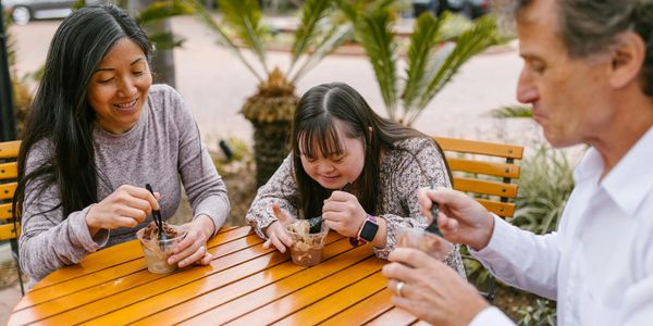 Three people enjoying ice cream outside at a wooden table.