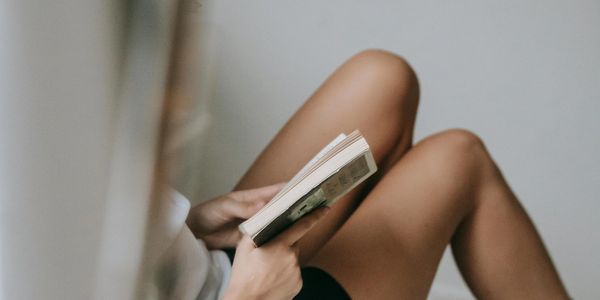 Person reading a book, focus on legs and hands.