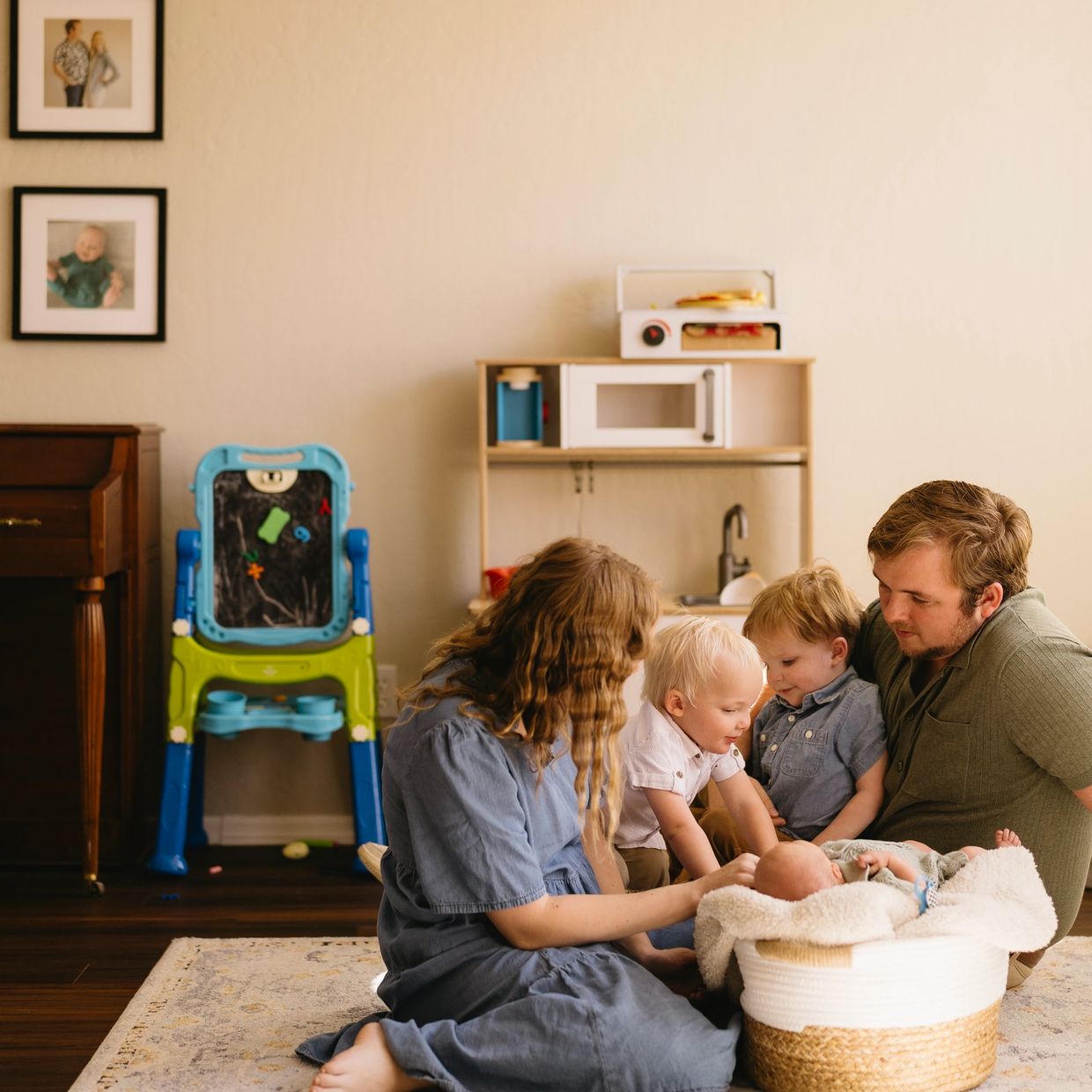 Family of five gathered on floor, focused on baby in a basket.