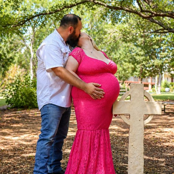 Pregnant couple sharing a kiss outdoors near a stone cross.