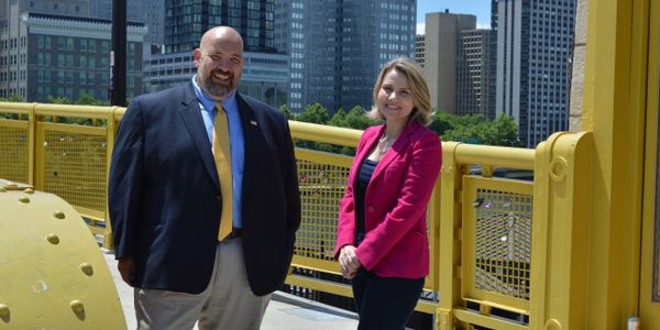 Two professionals posing on a yellow bridge in a cityscape backdrop.