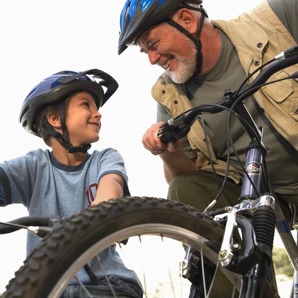 An elderly man preparing to ride bikes with his grandson. Both are wearing helmets and smiling.