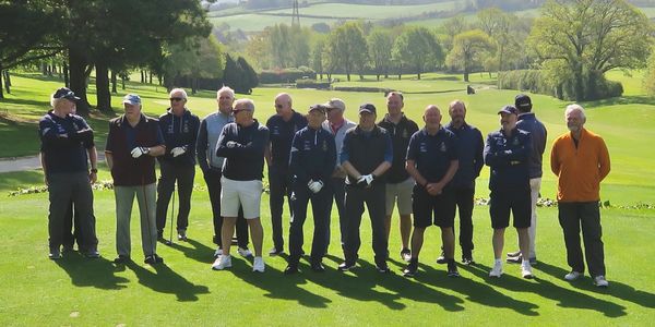 Group of men standing on a golf course on a sunny day.