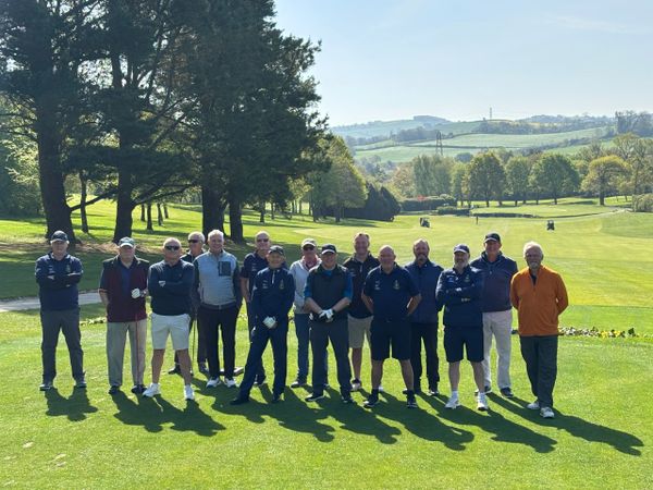 Group of men posing on a sunny golf course with rolling hills in the background.