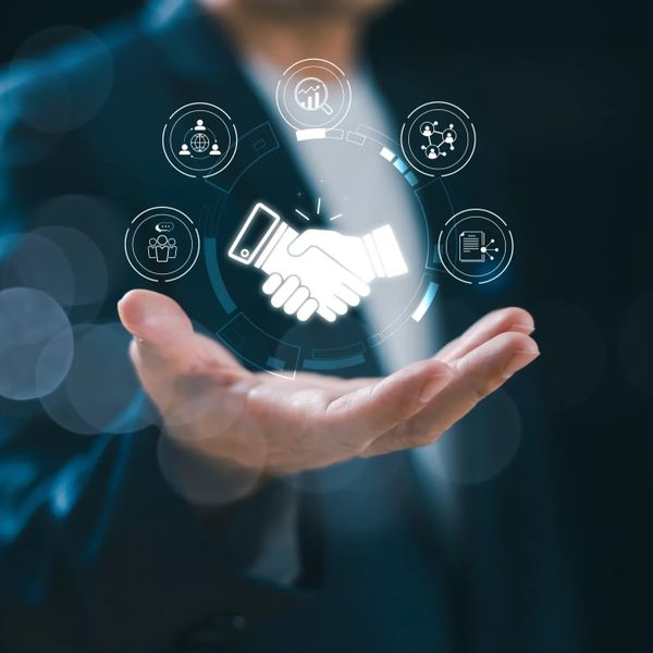 Hand holding digital handshake icon surrounded by business-related symbols.