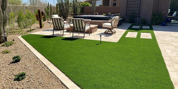 Lush green synthetic turf surrounding travertine patio used for spa and firepit landing. 