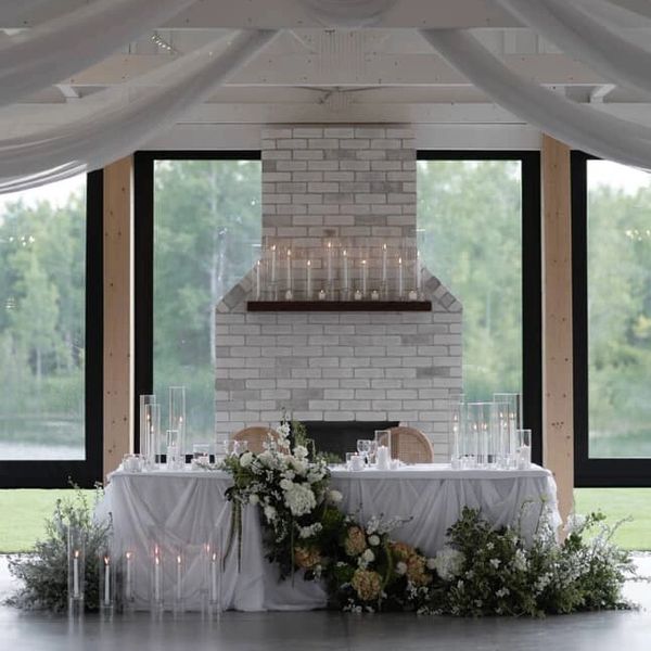 Elegant wedding table with floral decorations and candles by a white brick fireplace.