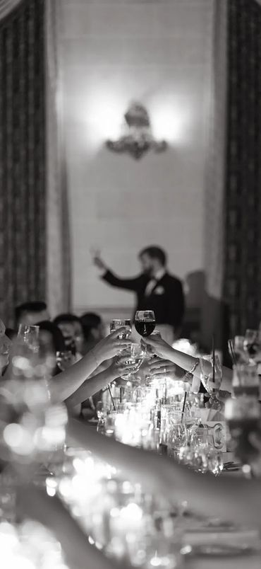 Guests raise glasses in a toast during a formal event, with a speaker blurred in the background.