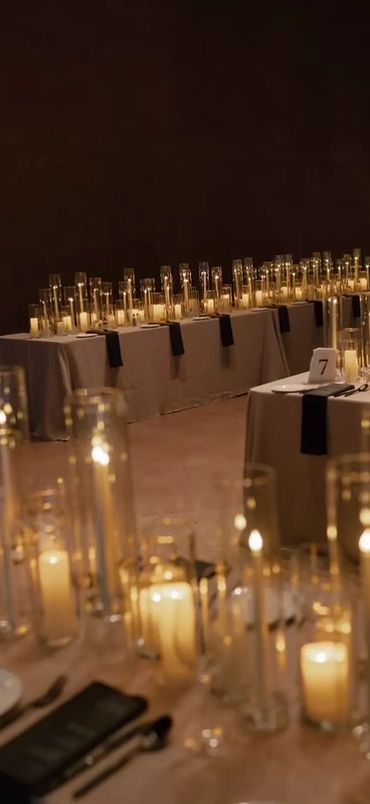 Elegant tables adorned with numerous lit candles in glass holders creating a warm ambiance.