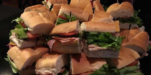 A pile of assorted deli sandwiches with lettuce and tomato.