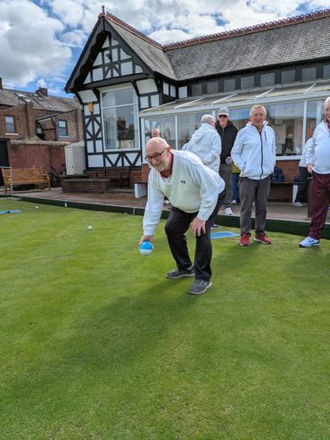 A man in white prepares to bowl on a green lawn with others watching.