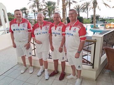 Four men in matching sports outfits standing by a pool with palm trees.