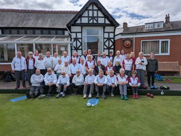 A large group of elderly people posing for a photo outside a building on a lawn bowling green.