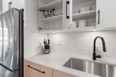 Modern kitchen countertop with open cabinets and stainless steel appliances.