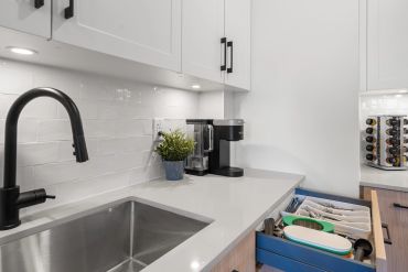 Modern kitchen corner with black faucet, coffee maker, and organized utensil drawer.
